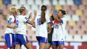 Four women in England football kits celebrating on the field after a match or goal.