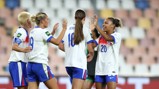Four women in England football kits celebrating on the field after a match or goal.