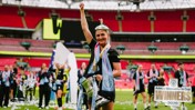 A Manchester City women's player raises the Adobe Women's FA Cup trophy with a team celebrating in the background. The stadium is filled with confetti and fans. The text 'Winners 2026' is prominently displayed.