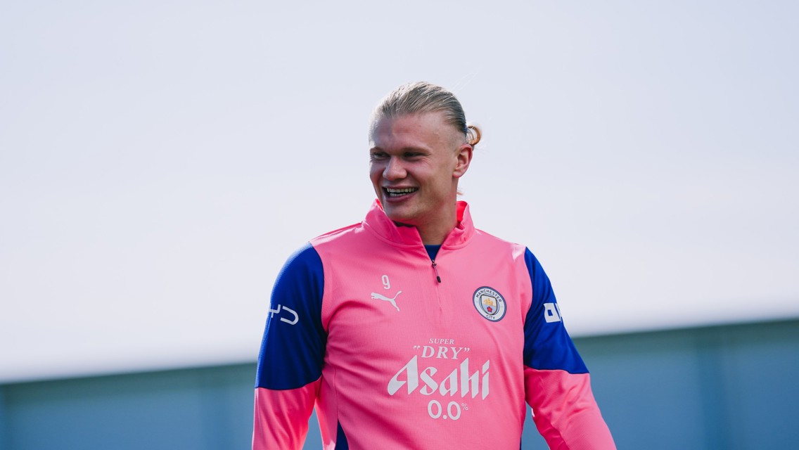 A person wearing a Manchester City training outfit with the number 9 and sponsorship details on the front. The training top is pink with blue sleeves and features the Manchester City crest.
