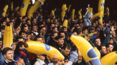 A large crowd at a stadium holding inflatable bananas as part of a celebration or event. The atmosphere appears energetic and lively.