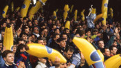 A large crowd at a stadium holding inflatable bananas as part of a celebration or event. The atmosphere appears energetic and lively.