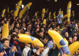 A large crowd at a stadium holding inflatable bananas as part of a celebration or event. The atmosphere appears energetic and lively.