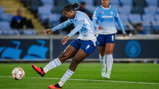 Two players from a women's soccer team in light blue jerseys in action during a match kicking a ball on the field.