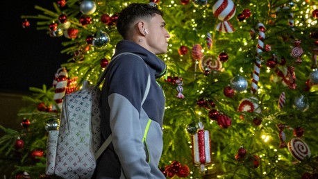 A person wearing a hoodie and carrying a Louis Vuitton backpack stands in front of a decorated Christmas tree with lights and candy ornaments.