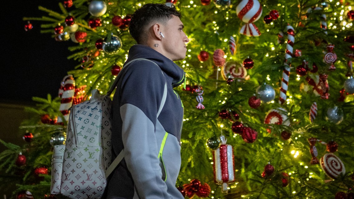 A person wearing a hoodie and carrying a Louis Vuitton backpack stands in front of a decorated Christmas tree with lights and candy ornaments.