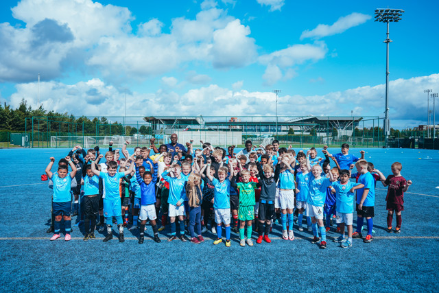 A group of children posing on a football field during a sunny day with blue sky.