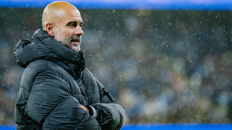 Person wearing a large puffy jacket standing in the rain with arms crossed.