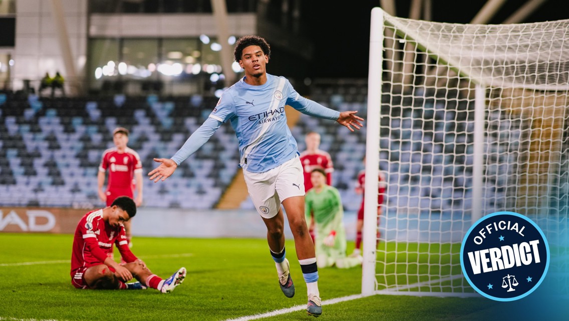 Football player in a blue Manchester City kit celebrates near the goal, while opposing players in red kits are nearby.