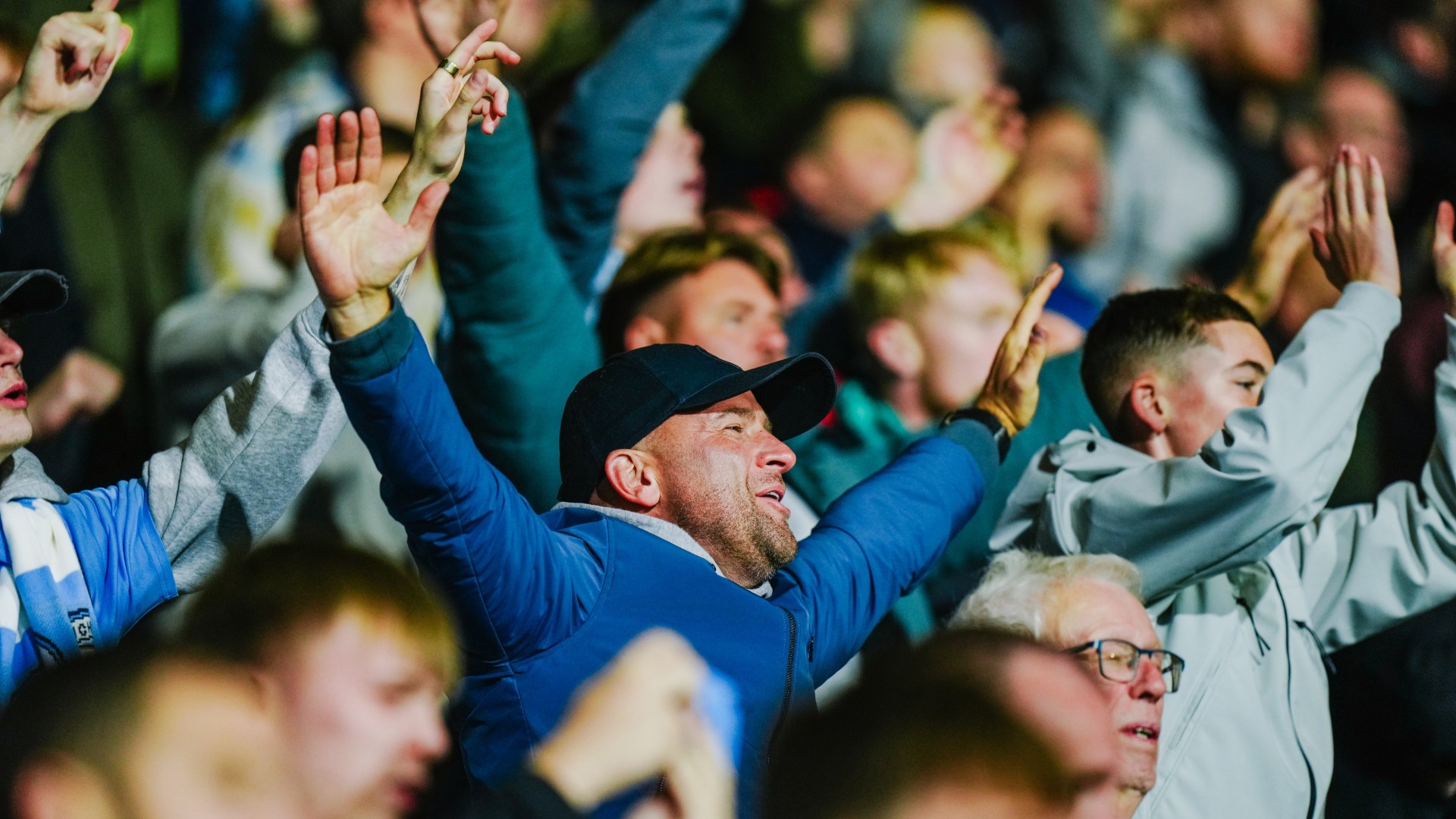 A group of people enthusiastically cheering, with their hands raised in the air, enjoying an event.