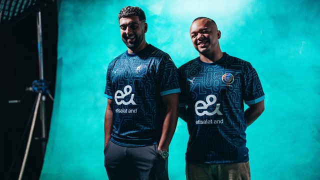 Two men wearing Manchester City esports jerseys with the etisalat and logo, standing in front of a blue background.