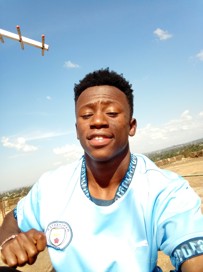 Person wearing a Manchester City jersey outdoors with a clear blue sky in the background.