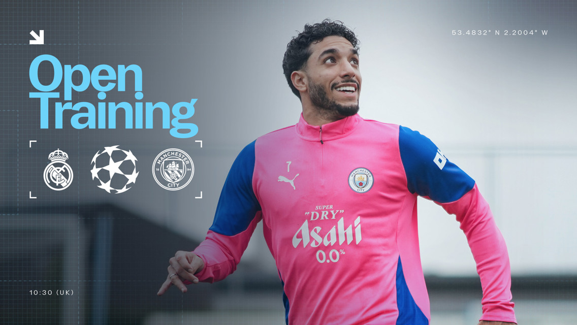 An image showing a Manchester City player during an open training session. The player is wearing a pink and blue training kit featuring the Manchester City logo, Puma logo, and Asahi sponsor. This is preparation for a match against Real Madrid.