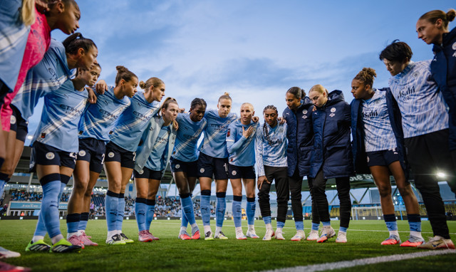 A group of soccer players in Manchester City uniforms huddling together on a field.