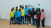 Group photo of young people and an adult wearing Manchester City attire at a community event, with a banner in the background.