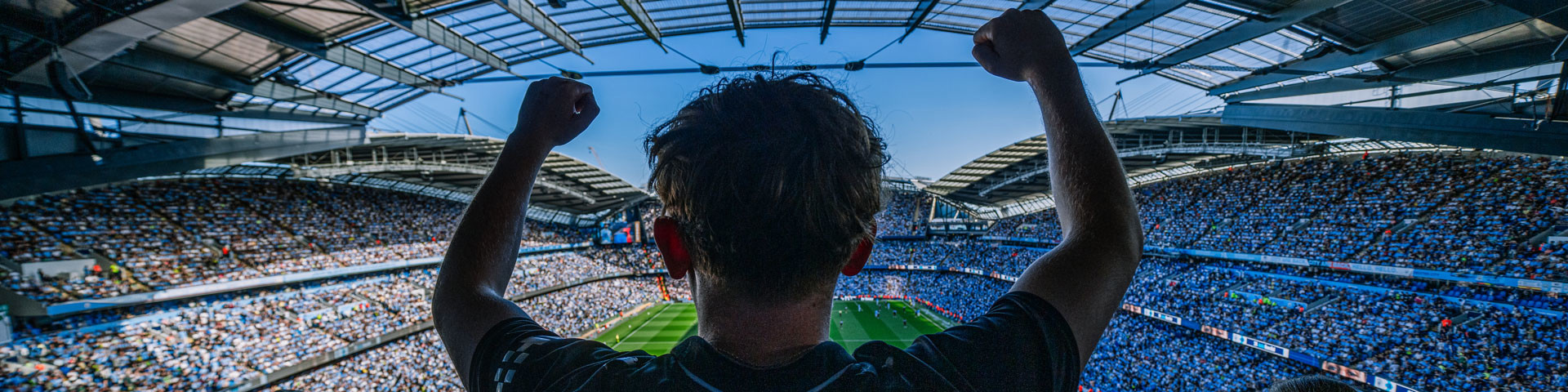 A football fan cheering with arms raised in a full stadium.