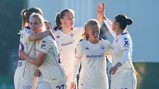 Five female athletes wearing white and purple soccer jerseys with sponsor logos celebrate and hug in a group. They appear joyful and engaged in team spirit.