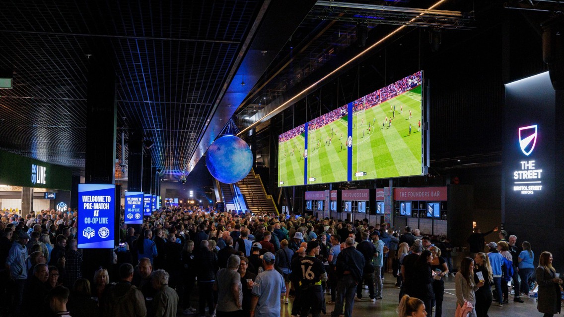 Large crowd at Co-op Live venue watching a sports event on big screens with multiple bars and signs around.