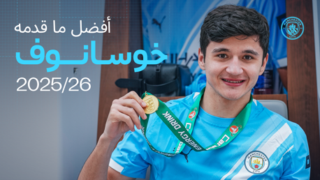 A player in a Manchester City jersey holding a medal with Arabic text and the year 2025/26.