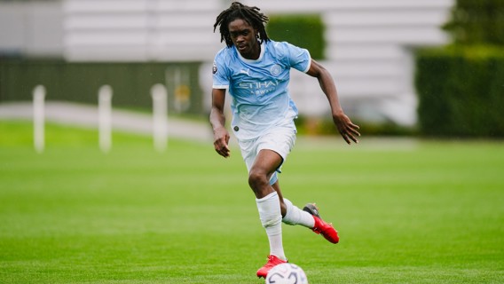 Football player in a Manchester City training kit dribbling a ball on a grass pitch.