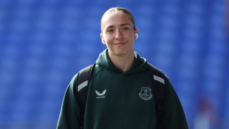 Person wearing an Everton hoodie with Castore branding, carrying a backpack, standing against a blue background.