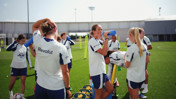Group of female soccer players wearing Manchester City training gear, drinking water, and relaxing on a field during training.