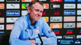 A person in a Manchester City tracksuit at a press conference table. Background includes various sponsor logos and a 'Manager's Preview' graphic. The Manchester City logo is visible on the tracksuit.