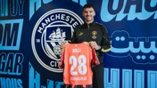 A person holding a Manchester City jersey with the name RULLI and number 28 inside the club's facility with Manchester City logo in the background.