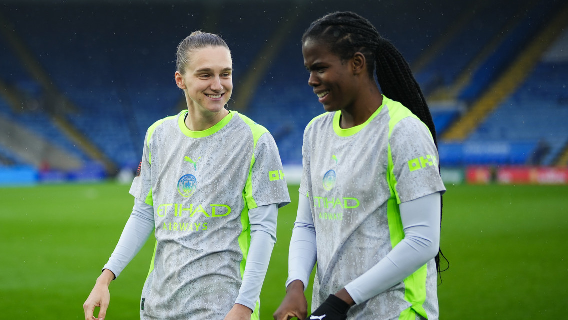 Two Manchester City women's team players in training gear on a football field.