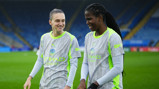 Two Manchester City women's team players in training gear on a football field.
