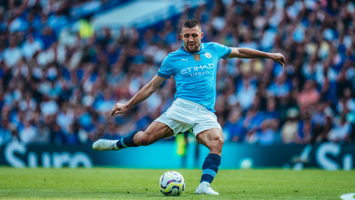 A soccer player in a Manchester City kit makes a pass during a match at a stadium.