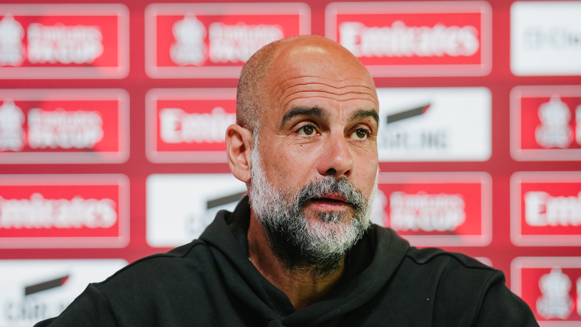 Man in a black hoodie speaking at a press conference with a background featuring Emirates FA Cup logos.