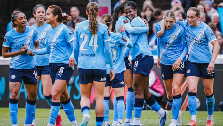 Manchester City Women's team celebrating on the field in blue jerseys during a match.