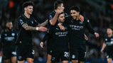 Football players in black Manchester City kits celebrating after a goal on the field.