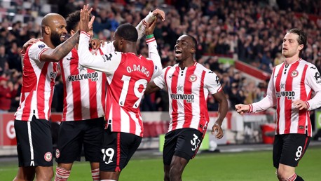 A group of Brentford FC players wearing their red and white striped jerseys celebrate on the field during a match.