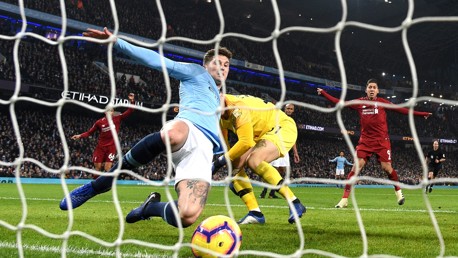 A Manchester City player in light blue makes a sliding goal-line clearance as Liverpool players in red look on at Etihad Stadium.