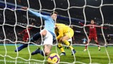 A Manchester City player in light blue makes a sliding goal-line clearance as Liverpool players in red look on at Etihad Stadium.