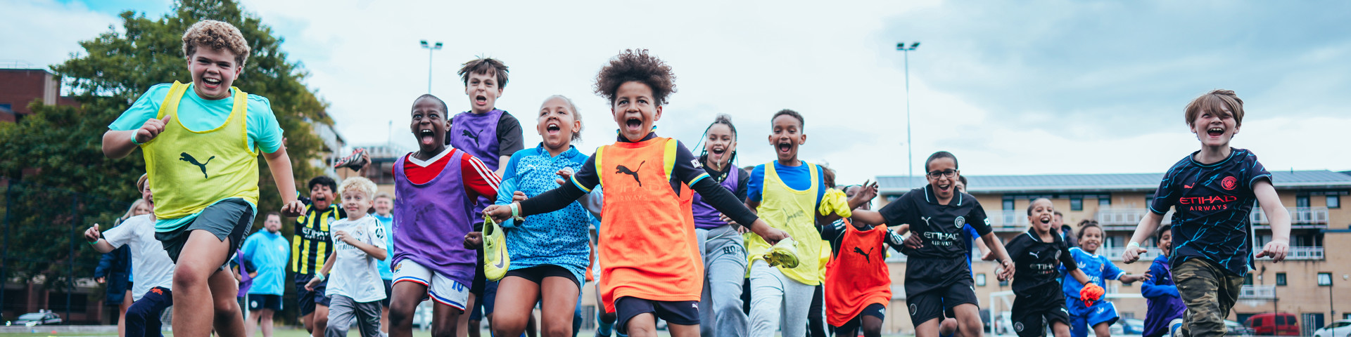 A group of children running on a soccer field wearing sports apparel. Some are wearing jerseys with logos.