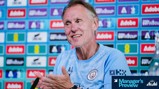 A person in a Manchester City shirt is clapping during a press conference. Behind them is a wall with various logos including Adobe. The image has a 'Manager's Preview' graphic in the corner.