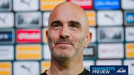 A person at a press event with sponsor logos in the background and a banner reading 'Manager's Preview'.