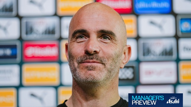 A person at a press event with sponsor logos in the background and a banner reading 'Manager's Preview'.