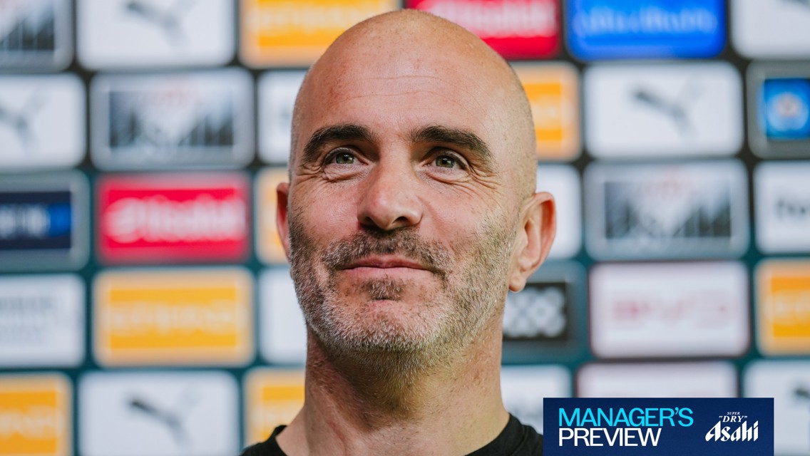 A person at a press event with sponsor logos in the background and a banner reading 'Manager's Preview'.