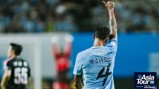 Football player in a light blue jersey with number 4 raises a finger. The shirt has 'experience abu dhabi' text. Backdrop of an indoor stadium. Asia Tour '26 logo in the corner.