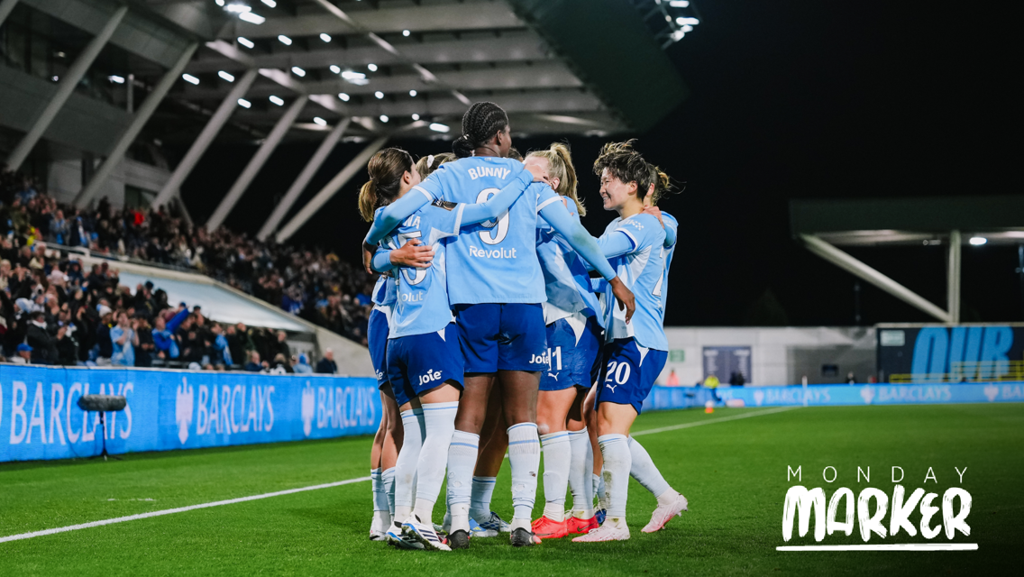 Soccer players wearing light blue jerseys celebrating a goal on the field. The stadium is full with spectators, and 'Monday Marker' text is visible.