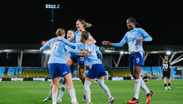 Group of Manchester City Women's players celebrating a goal on the field at night.