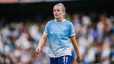 A Manchester City female player wearing the team's sky blue kit with the number 11 visible, walking on the field during a match.