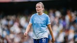 A Manchester City female player wearing the team's sky blue kit with the number 11 visible, walking on the field during a match.