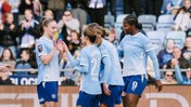 Manchester City women's team players in blue jerseys celebrate a goal with high-fives on the field during a match.