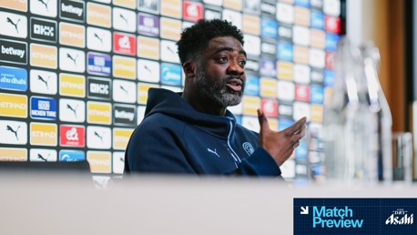 A person, possibly an athlete or coach, is speaking at a press conference with a sponsor-laden background. The words 'Match Preview' and 'Asahi' are present on the bottom right corner.