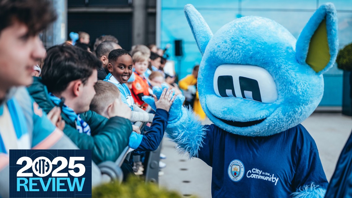 A blue mascot in a Manchester City shirt high-fives children at an event. The background includes several spectators wearing team jerseys. The text '2025 Review' is also visible.